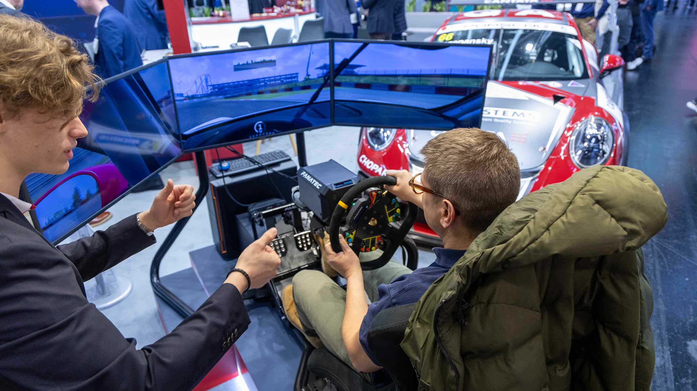 Two men control a car simulator at an exhibition at Embedded World