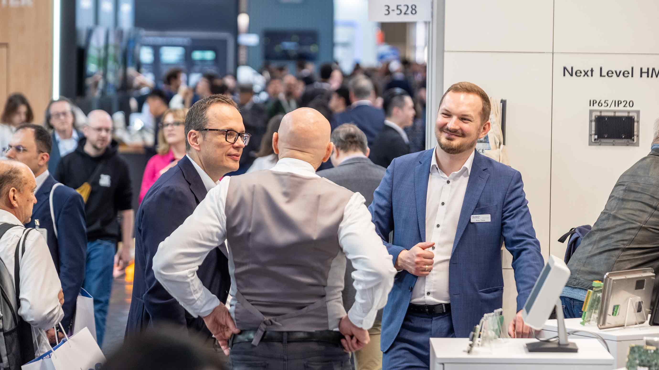 Several trade fair attendees talking at an exhibitor booth in a crowded exhibition hall.