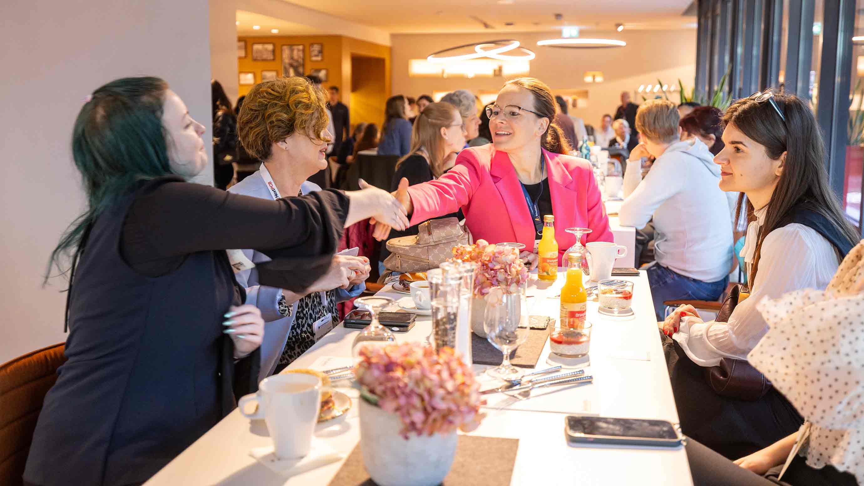 Two participants greet each other with a handshake at a table of women networking